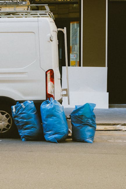 A disorganized collection of overflowing rubbish bins and scattered waste consisting of paper bags, cardboard boxes, plastic packaging, and black plastic trash bags, situated on a paved urban area nea